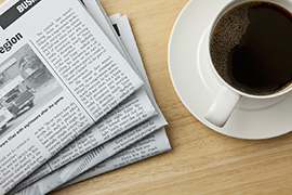 A newspaper sits on a table next to a cup of coffee