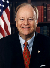 Official U.S. Senator potrait in suit and tie, with American flag behind him.