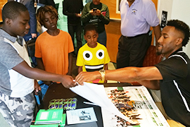 Stetson basketball player Divine Myles signs Hatter posters for boys.