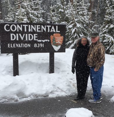 Wendy and Richard Libby stand in light snowfall at the Continental Divide sign in Yellowstone National Park