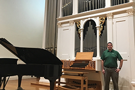 Chris Cloudman stands on stage of Lee Chapel with organ, piano