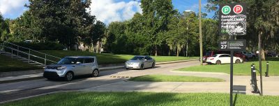 Cars drive down a street passed a red and green zone for resident and commuter parking.