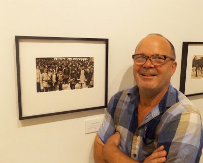 Andrew Murray Howe stands beside framed 1909 photo of Moscow Thieves Market in Hand Art Center