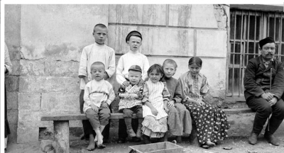 A collection of poor children around a bench as stern Russian man looks on