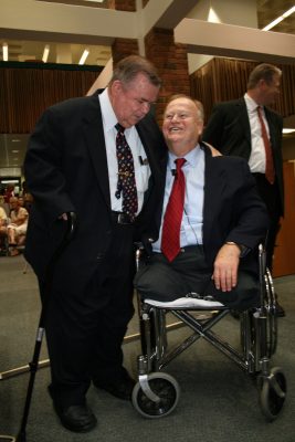 Dr. T. Wayne Bailey has his arm around Max Cleland seated and smiling in a wheelchair.