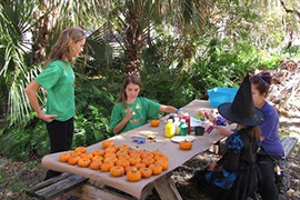 Students sit at pumpkin table making crafts with little pumpkins