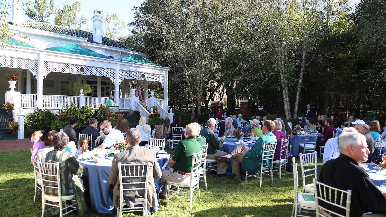 Crowd shot, seated at outdoor tables behind the President's Home.