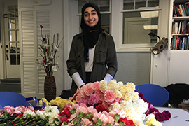 Fatima Asad poses in front of a pile of flowers on a table in Stetson's Cross Cultural Center