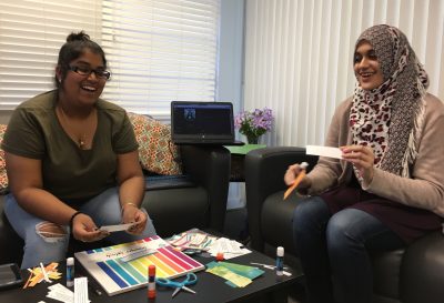 Muslim Student Association members Kristin Ramkissoon, left, and Zainab Nadeem sit on couches in the Cross Cultural Center with art supplies on a coffee table in front of them.