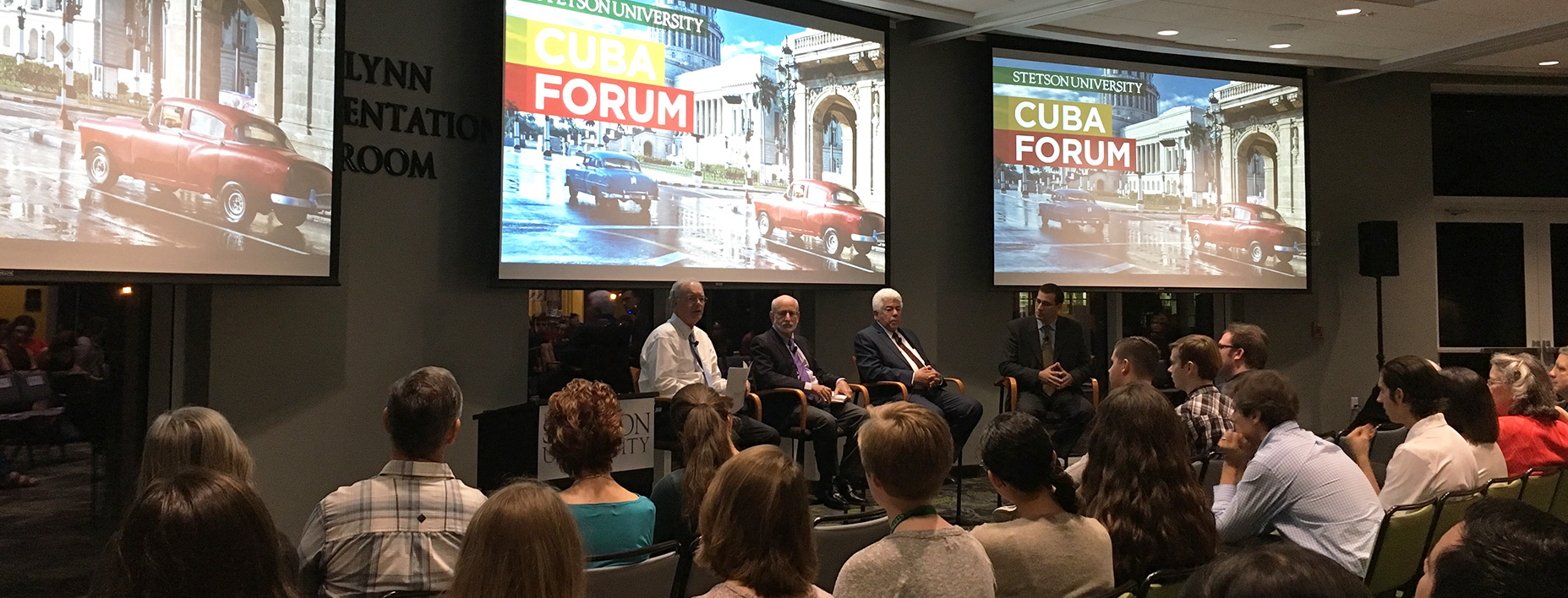 The crowd is seated in the Rinker Welcome Center and listens to the three panelists and moderator at the front of the room.