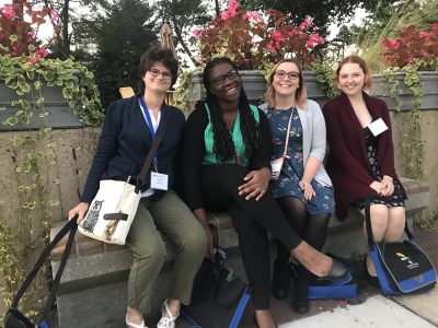 The four students sit on a bench in what looks like a garden with big smiles.