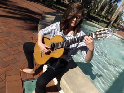 Lauren Baucum plays a guitar seated beside Holler Fountain on Stetson University's DeLand campus.