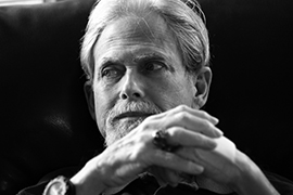 Black and white portrait of Michael Fronk seated in a recliner chair in his home.