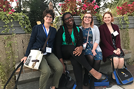 The four students sit together outside on a bench with all their convention materials.