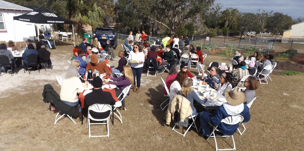 Fold-out tables are filled with diners next to the community garden for the dinner.
