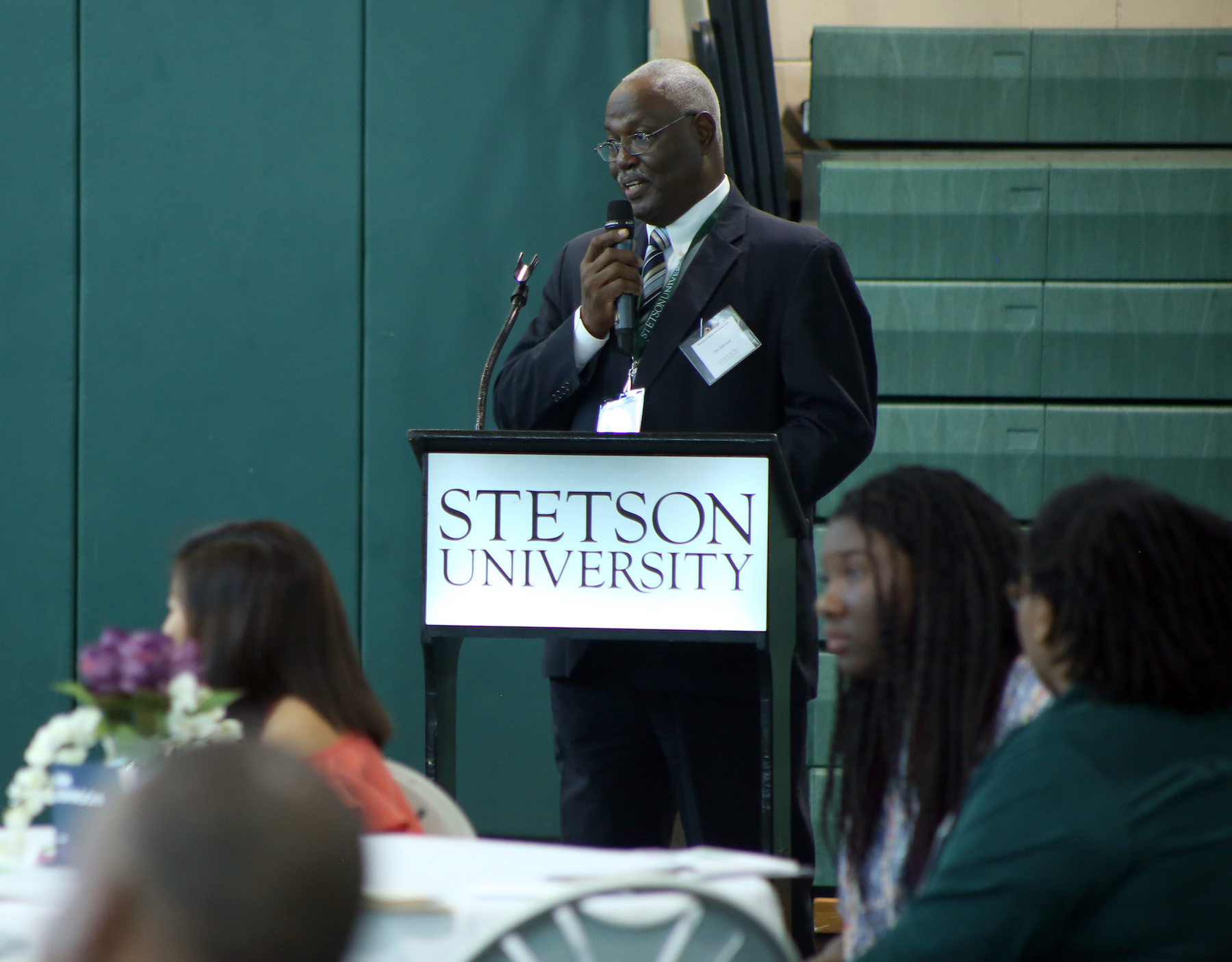 Jim Johnson stands at a podium with a microphone in hand, speaking to people in attendance.