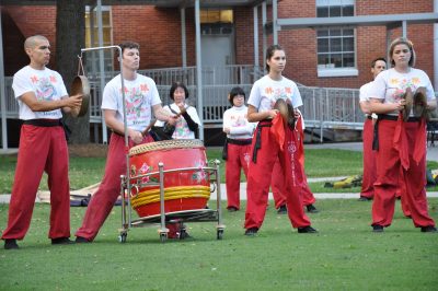 Four musician/dancers in Asian bright red and white outfits perform on the Stetson Green.