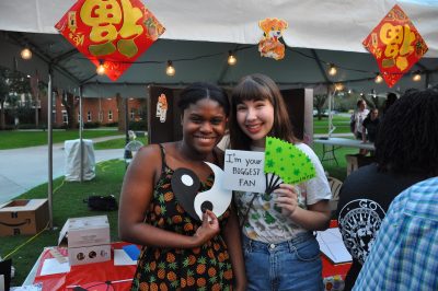 Two women stand holding little signs and crafts made at festival.