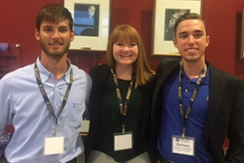 Three students pose arm and arm at conference