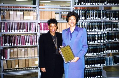 The two women stand in front of bookshelves of law books.
