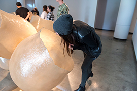 A woman bends and leans into one of the fiberglass pods representating a bumble bee nest.