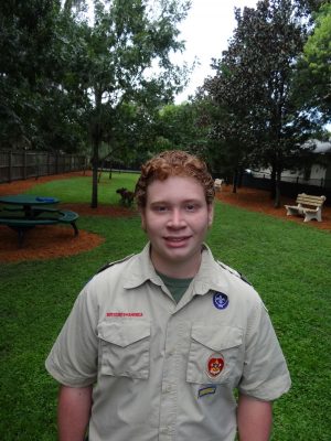 Corey Sipe stands in his Boy Scout uniform in the nice and new dog park with landscaping.
