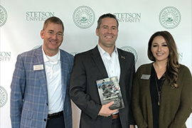 Group shot of three of them standing against a backdrop with the Stetson logo; Waltz is holding his book