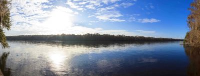 a panorama shot of a river with land and trees in the distance