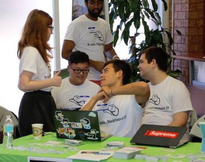 A group of students sit around a table and computers, talking.