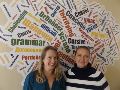 The two professors stand in front of a collection of English and Russian words written in bright primary colors.