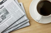 cup of coffee on a table next to print newspaper
