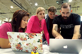 The four of them are hunched over laptops looking at the screen.