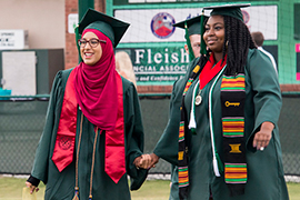 Two women hold hands as they walk onto the field.