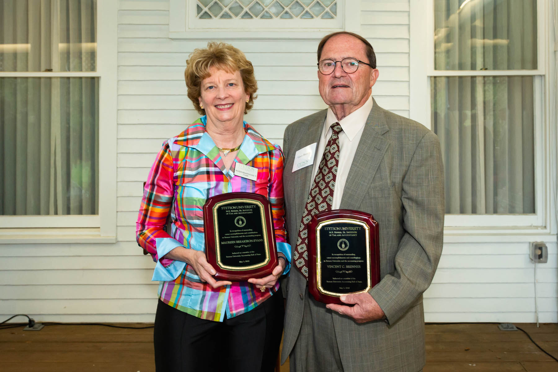 The two stand side by side on a porch holding their plaques.