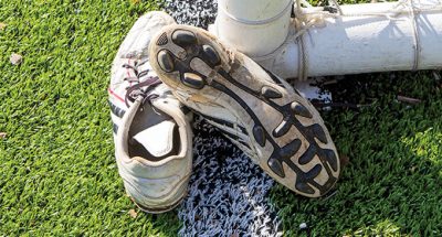 dirty cleats sit on the grass next to a soccer goal