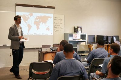 Andrew Eisen stands in front of the class with a powerpoint slide.