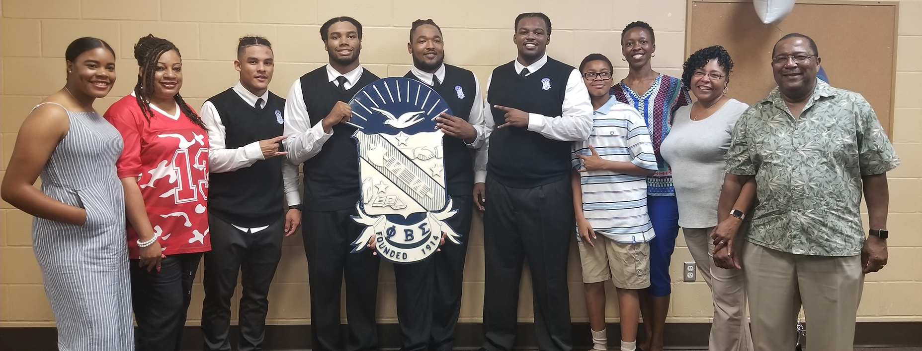 Long group shot of family with the four young men as they hold a banner with the fraterniy's crest.