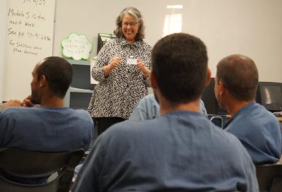 Wendy Libby smiles and laughs while standing in the front of the class of incarcerated students.