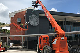 Two pieces of heavy equipment lift the seal and workers in place to attach the seal to the building.