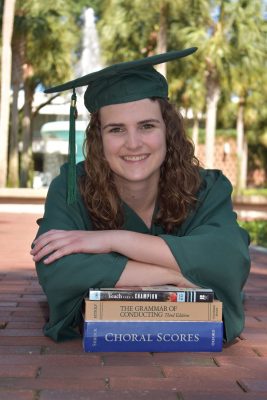 Erin Scully leans over a stack of textbooks in a Stetson green cap and gown.