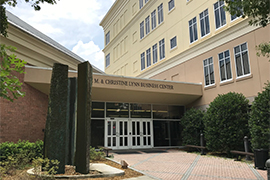 Exterior of entrance of building with a sculpture fountain and the name over glass doors.