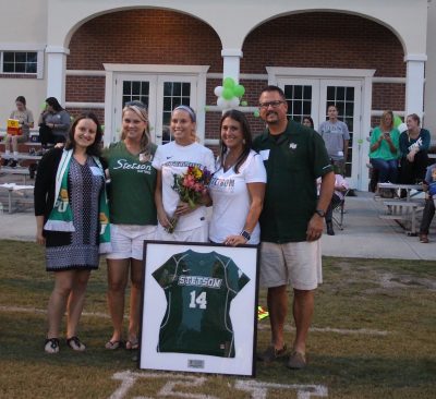 Meredith Sinak stands with family and a framed Team Jersey outside the Stetson Athletic Training Center on campus.