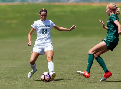 Meredith Sinak kicks a soccer ball during a match as an opposing player rushes toward her.