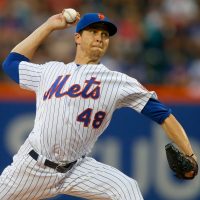 Jacob deGrom gets ready to throw a pitch on the field in uniform.