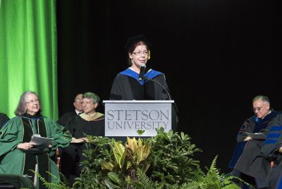 Megan O'Neill at the podium as President Wendy Libby and other college administrators listed on the stage.
