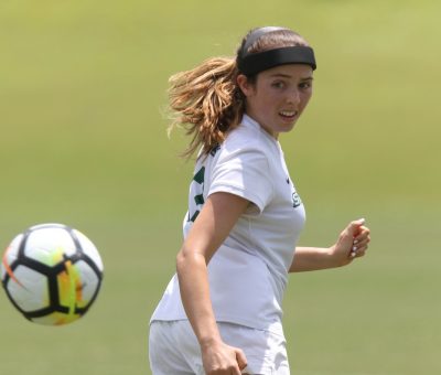 Jordan Ross runs on the soccer field, looking over her shoulder at an approaching soccer ball.
