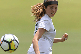 Jordan Ross runs on the soccer field, looking over her shoulder at an approaching soccer ball.