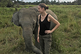 Kate Welch stands with a baby elephant in a grassy area.
