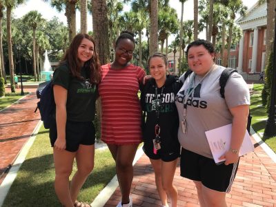 The four students stand arm in arm in palm court