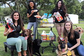 Four students pose with various pet items and service dogs